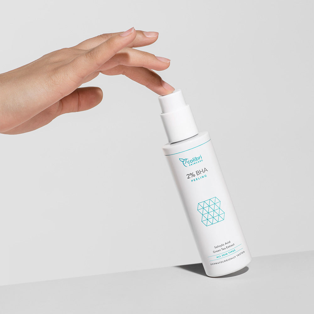Hand greift nach einem weißen Fläschchen mit 2% BHA Peeling auf hellem Hintergrund.