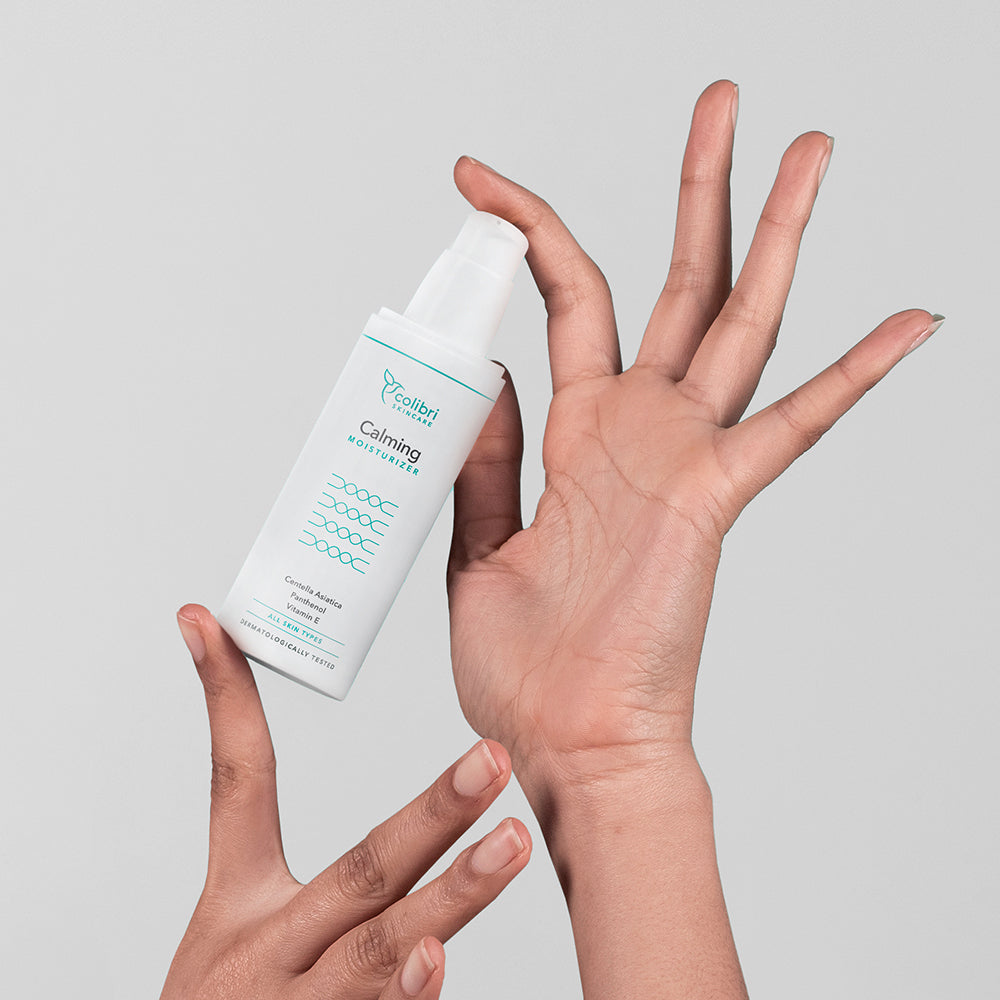 Zwei Hände halten eine Flasche Feuchtigkeitscreme vor einem grauen Hintergrund.