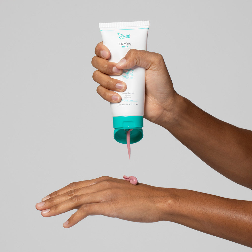 Eine Person trägt rosa Creme aus einer Tube auf den Handrücken auf.