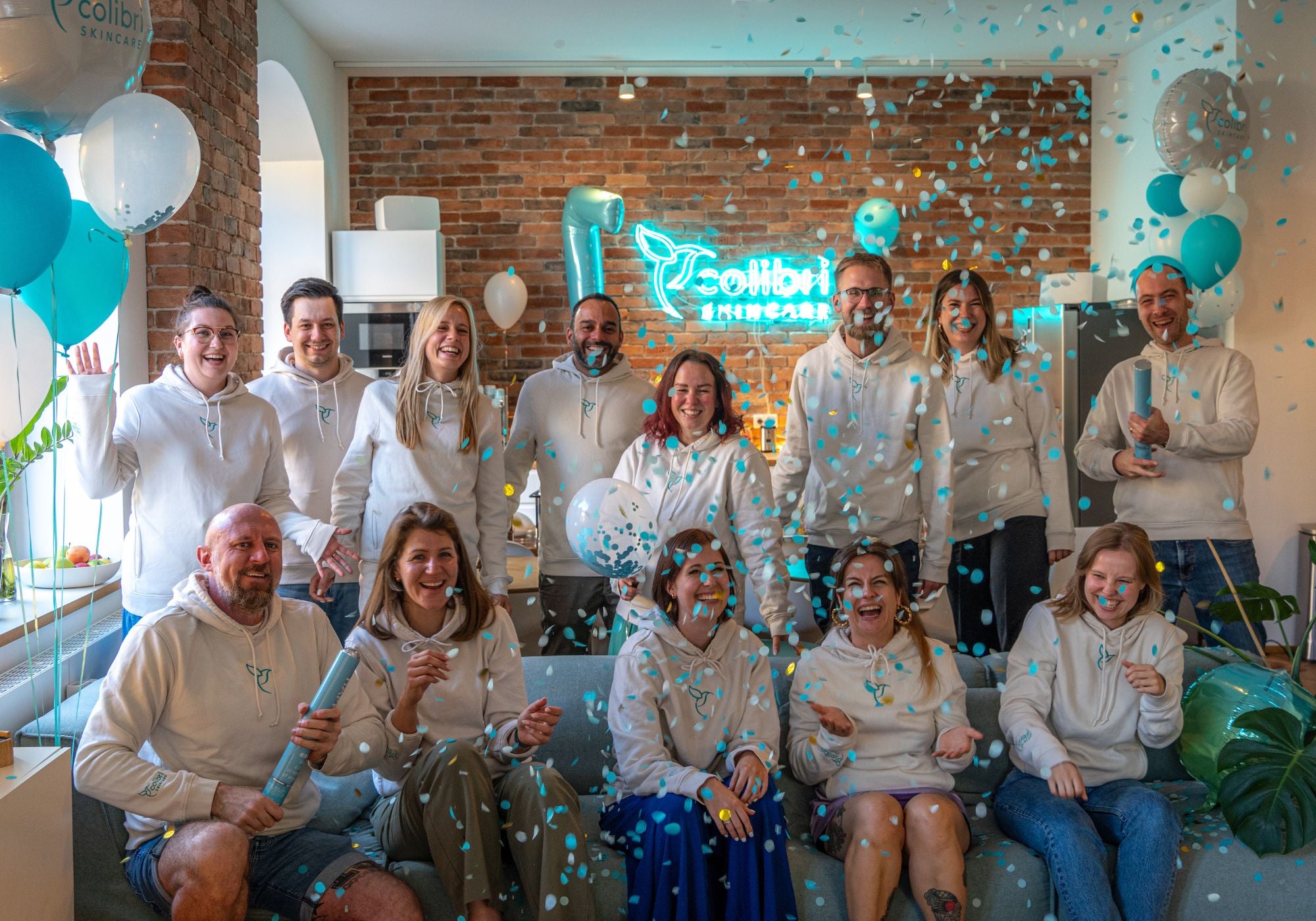 Eine Gruppe von Menschen in weißen Hoodies feiert mit blau-weißem Konfetti in einem festlich dekorierten Raum.