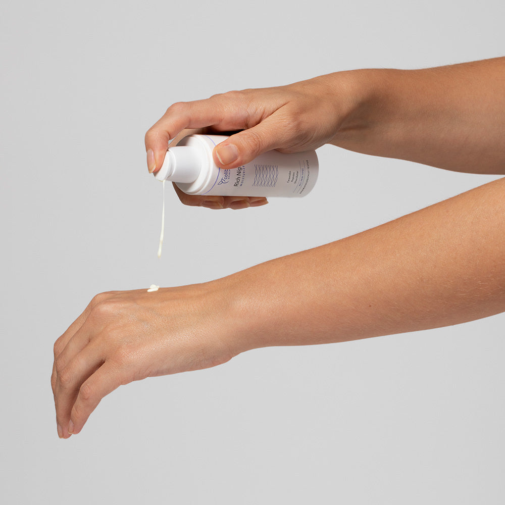 Eine Person trägt Creme aus einer Flasche auf den Handrücken auf.
