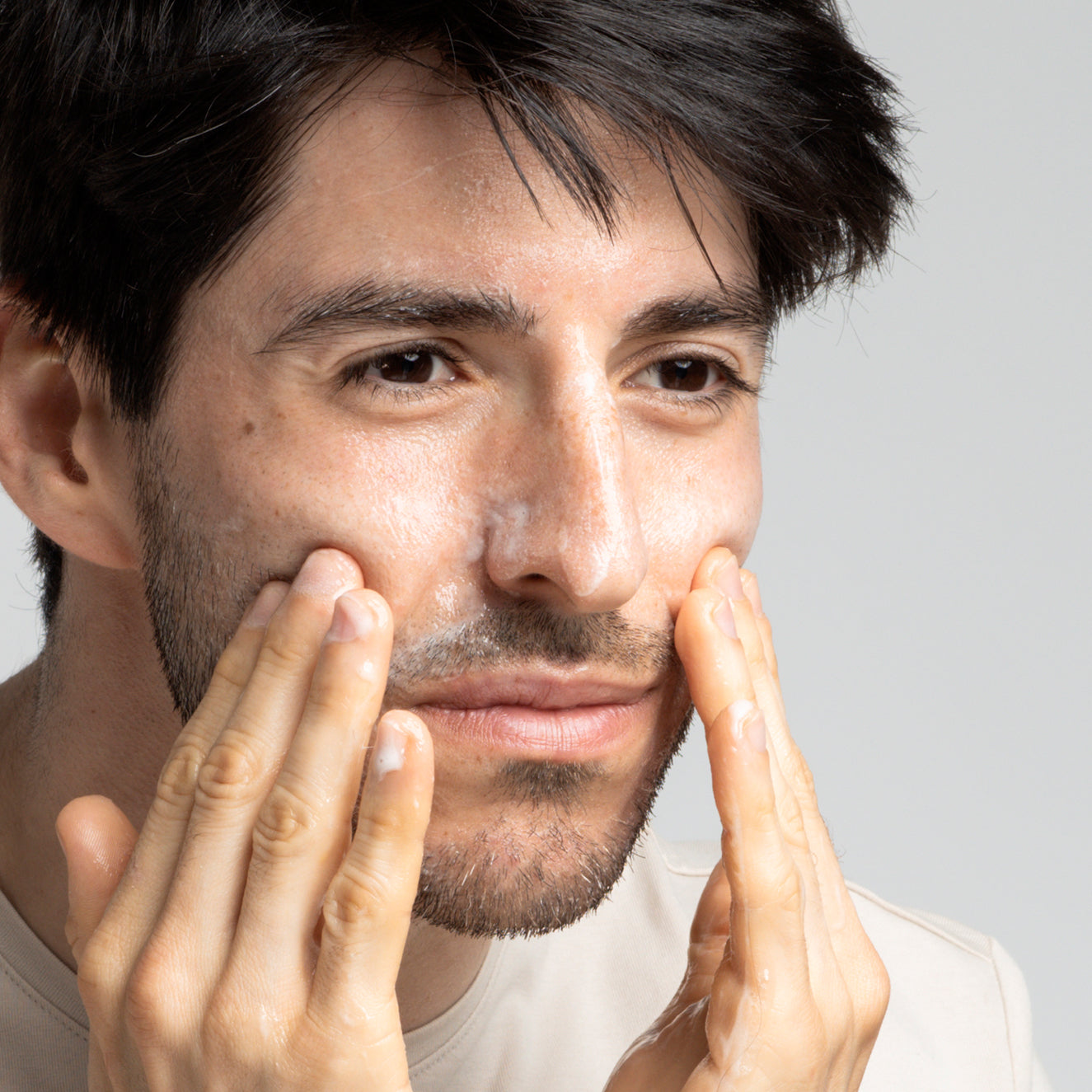 Ein Mann reinigt sein Gesicht mit Gesichtsreinigungsschaum und massiert sanft seine Wangen mit den Händen.