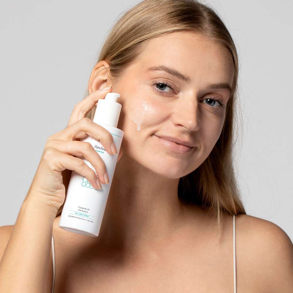 Frau trägt Hautpflegecreme auf ihr Gesicht auf, während sie eine Flasche in der Hand hält.