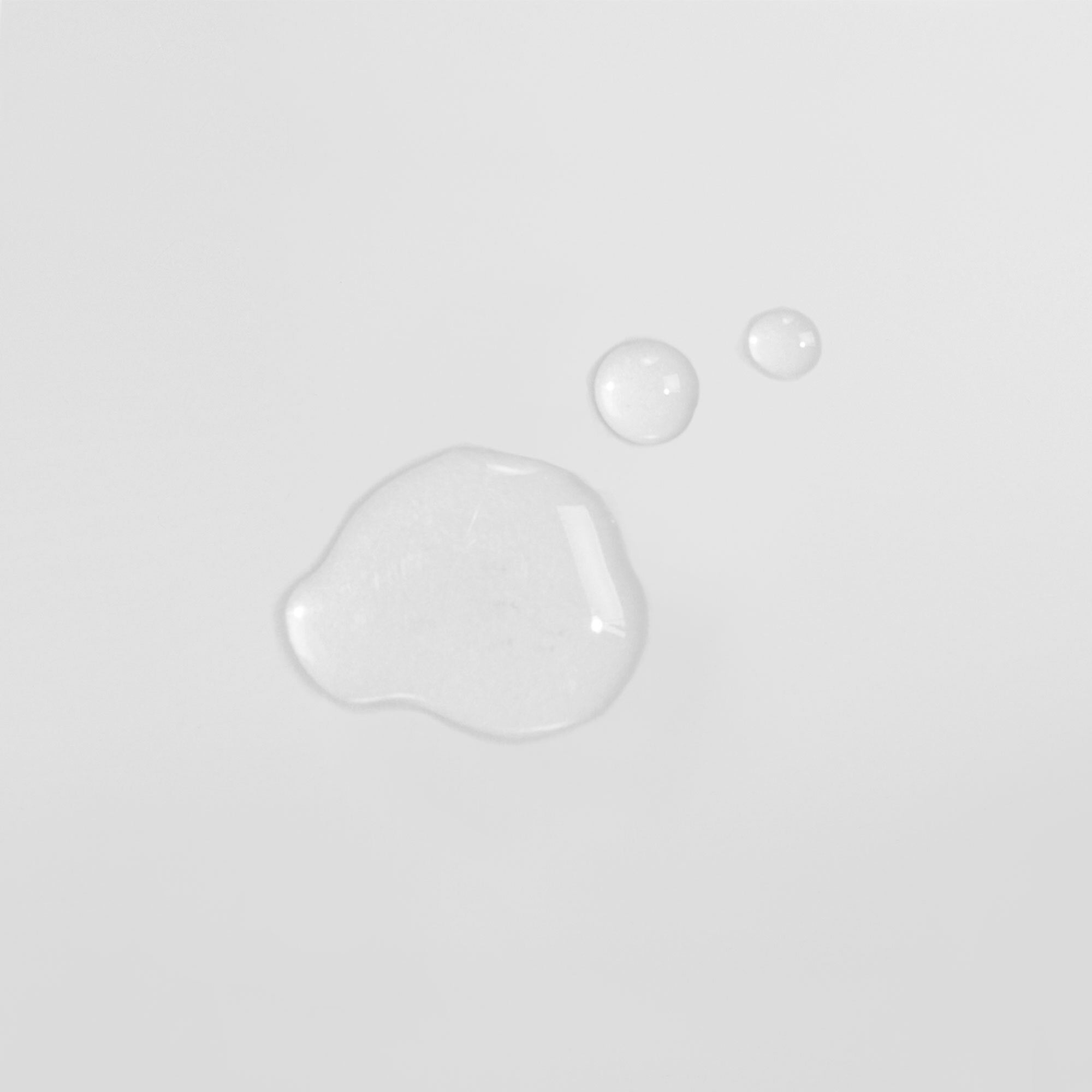 Drei transparente Flüssigkeitstropfen auf einem weißen Untergrund.