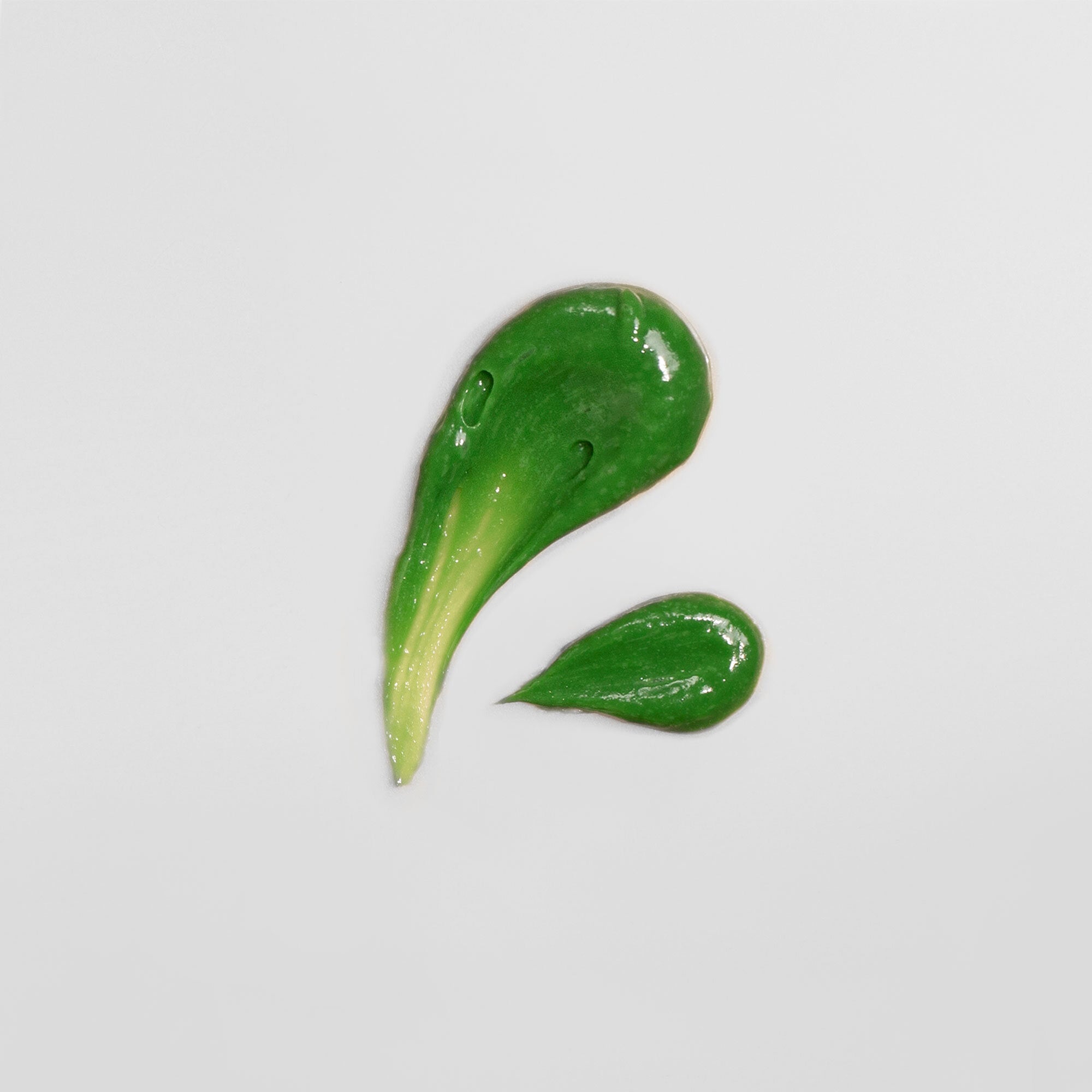 Grüne, cremige Textur tropfenförmig auf weißem Hintergrund verteilt.