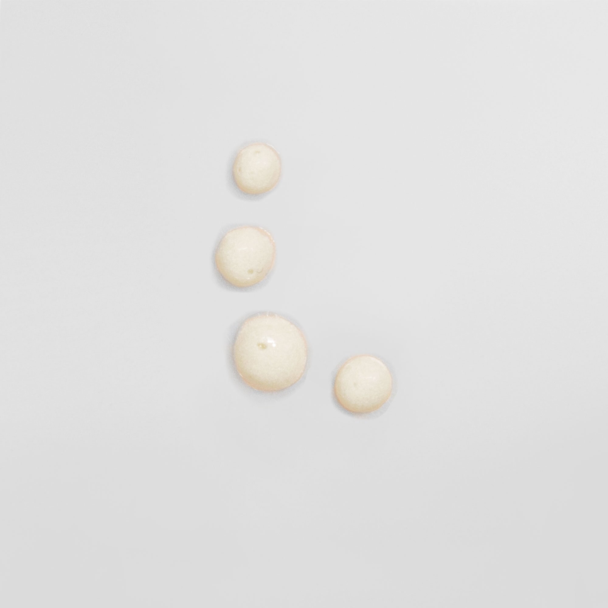 Vier kleine Tropfen einer transparenten Flüssigkeit auf einer grauen Oberfläche.