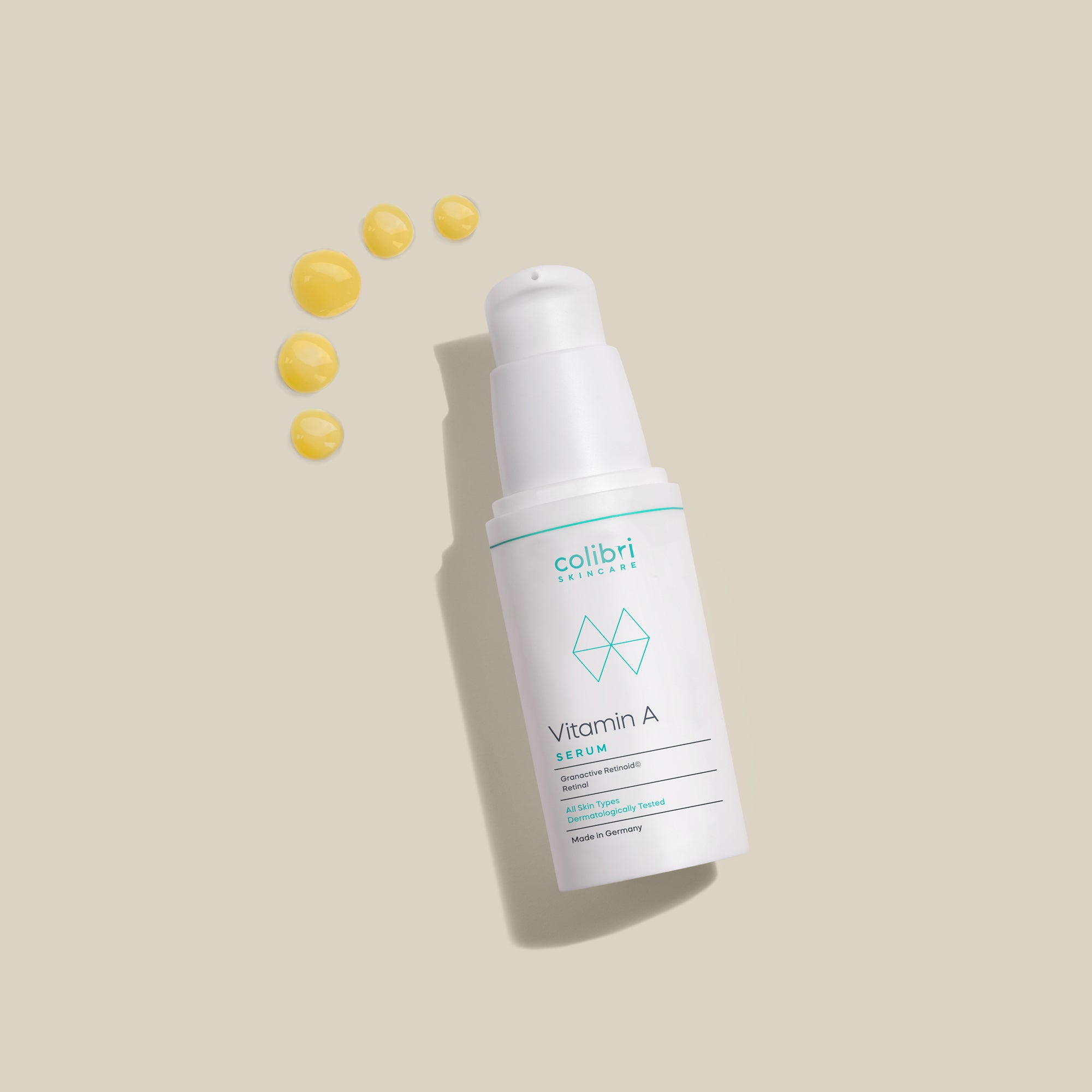 Weißer Spender mit Vitamin A Serum auf beigem Hintergrund, daneben gelbe Flüssigkeitstropfen.