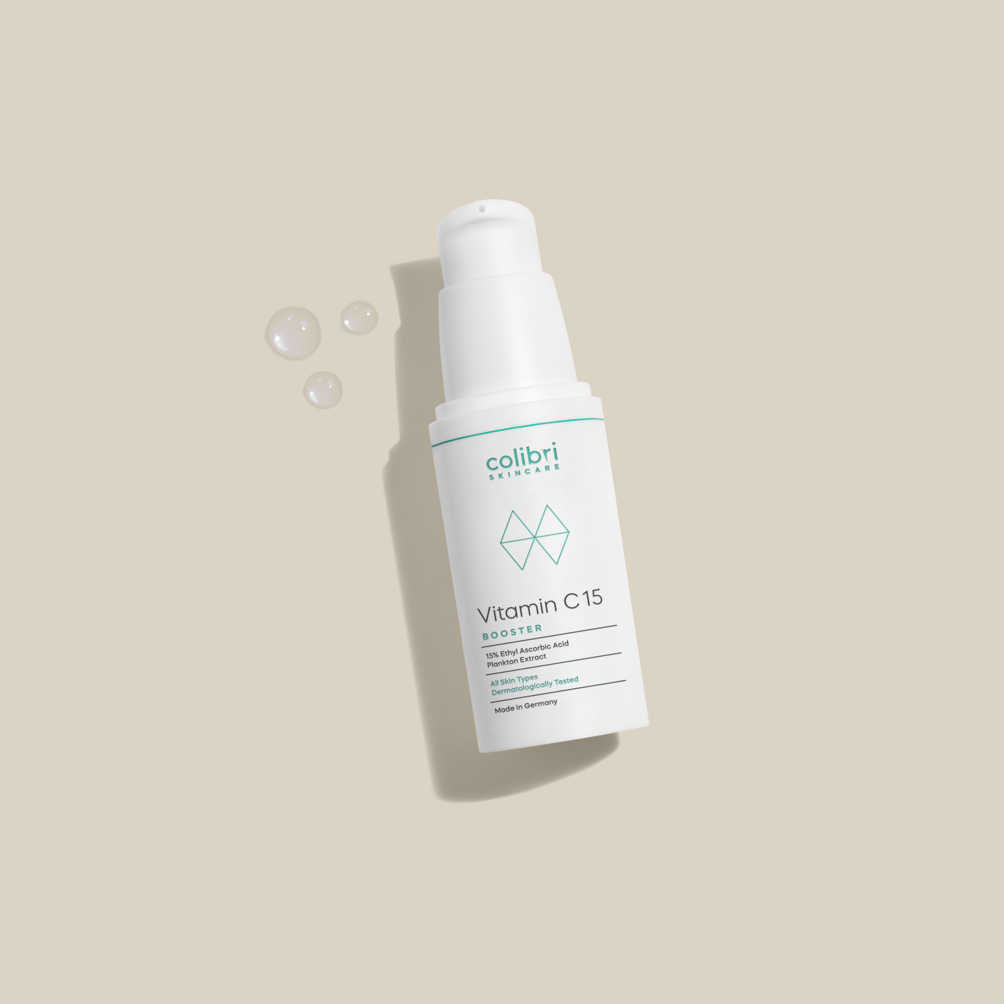 Flasche mit Vitamin C15 Booster von colibri skincare auf beigem Hintergrund mit ein paar Tropfen daneben.