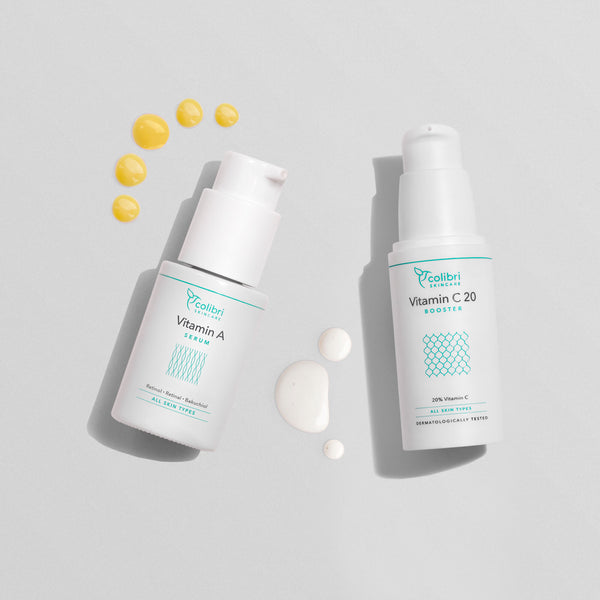 Zwei Fläschchen Hautserum mit Vitamin A und Vitamin C20, umgeben von kleinen Tropfen auf einem grauen Hintergrund.
