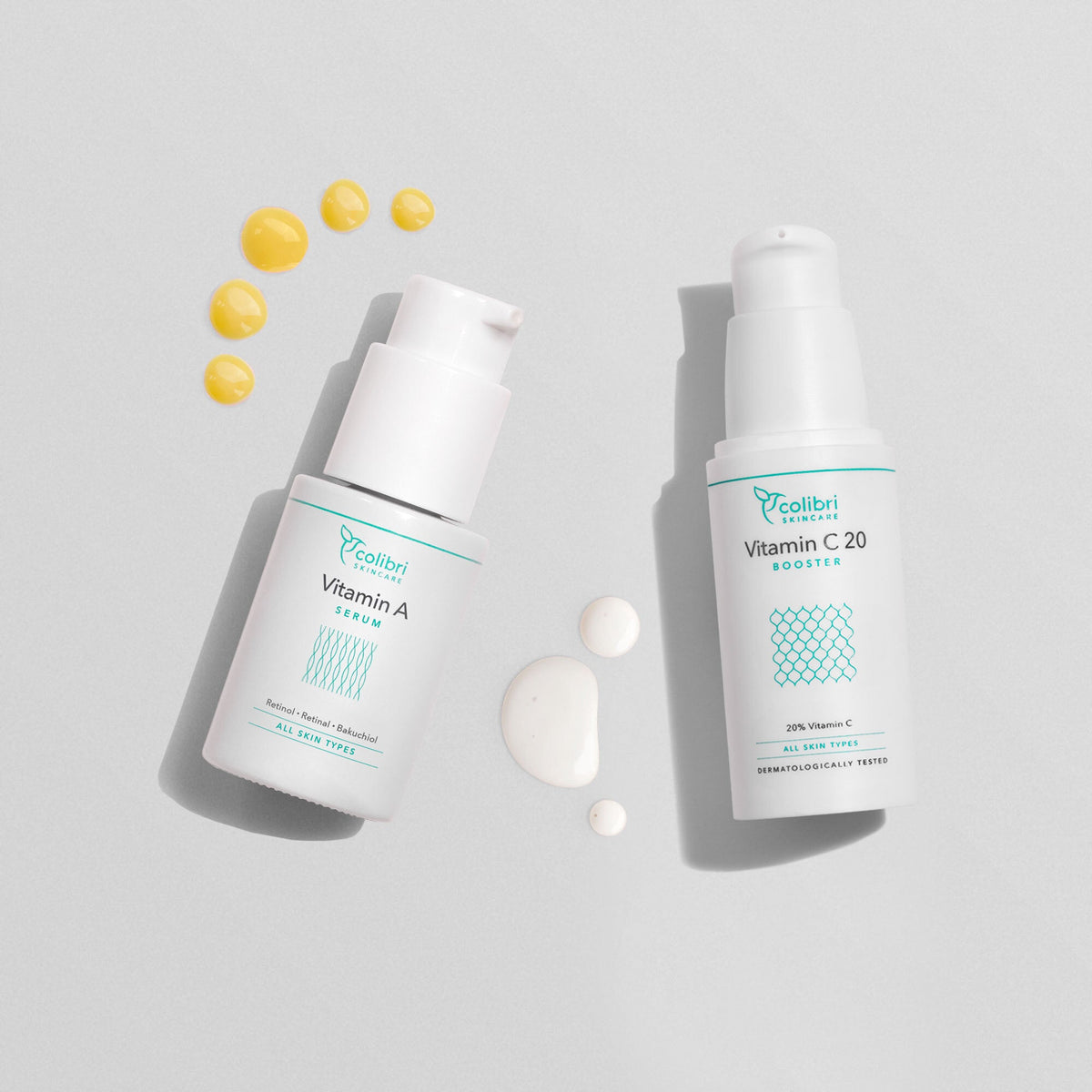 Zwei Fläschchen Hautserum mit Vitamin A und Vitamin C20, umgeben von kleinen Tropfen auf einem grauen Hintergrund.