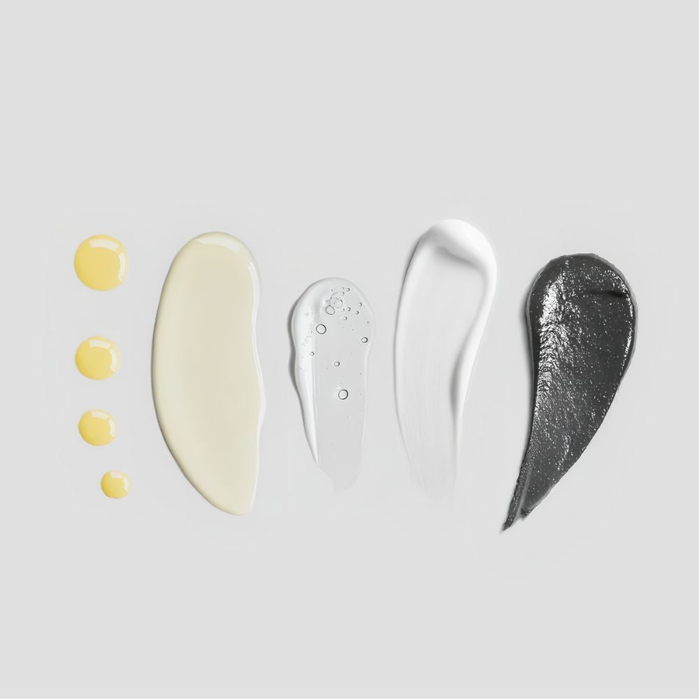 Fünf verschiedene Creme- und Serumkleckse in Gelb, Beige, Transparent, Weiß und Grau auf grauem Hintergrund.