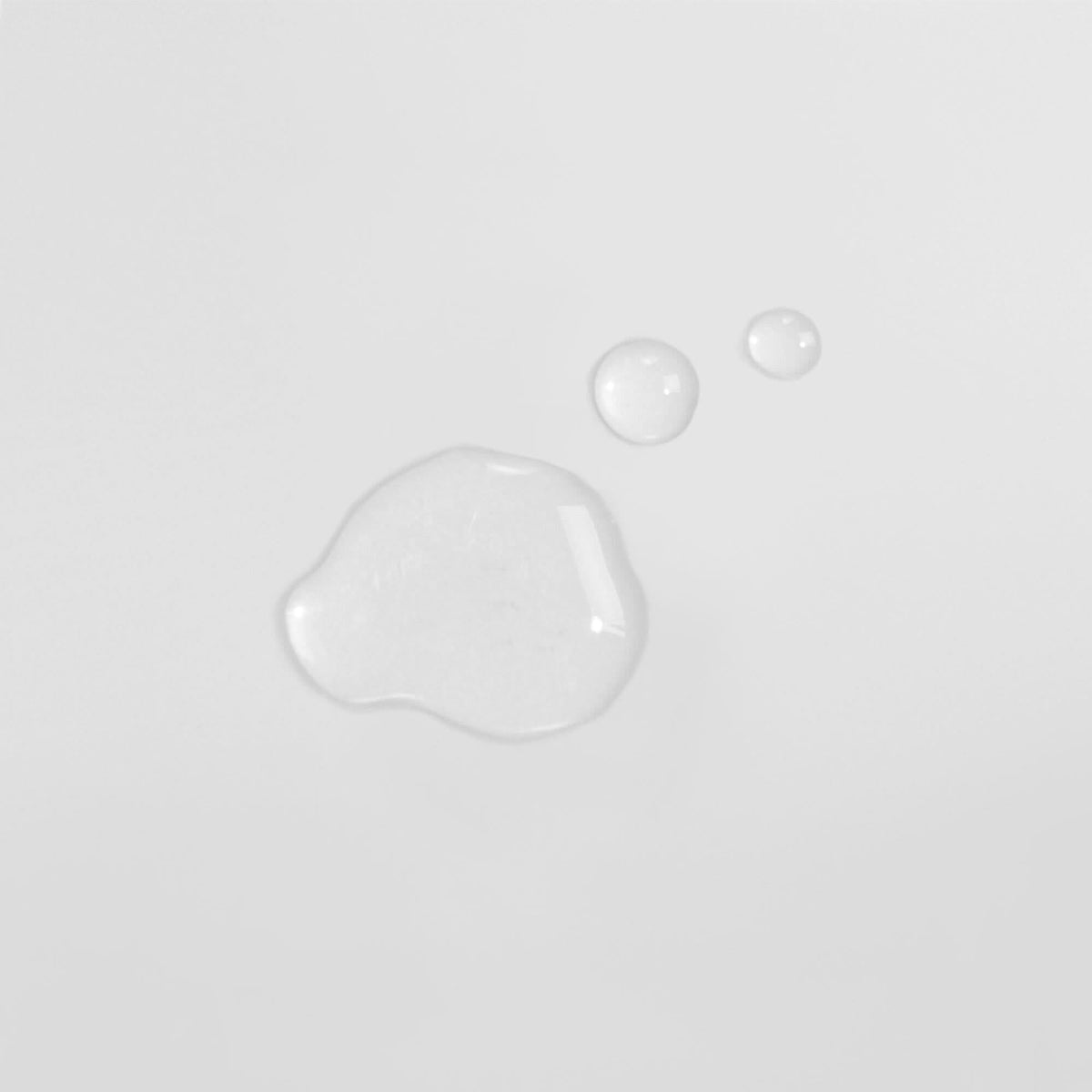 Drei Wassertröpfchen auf einer weißen Oberfläche, zwei kleinere oben rechts und ein größeres links unten.